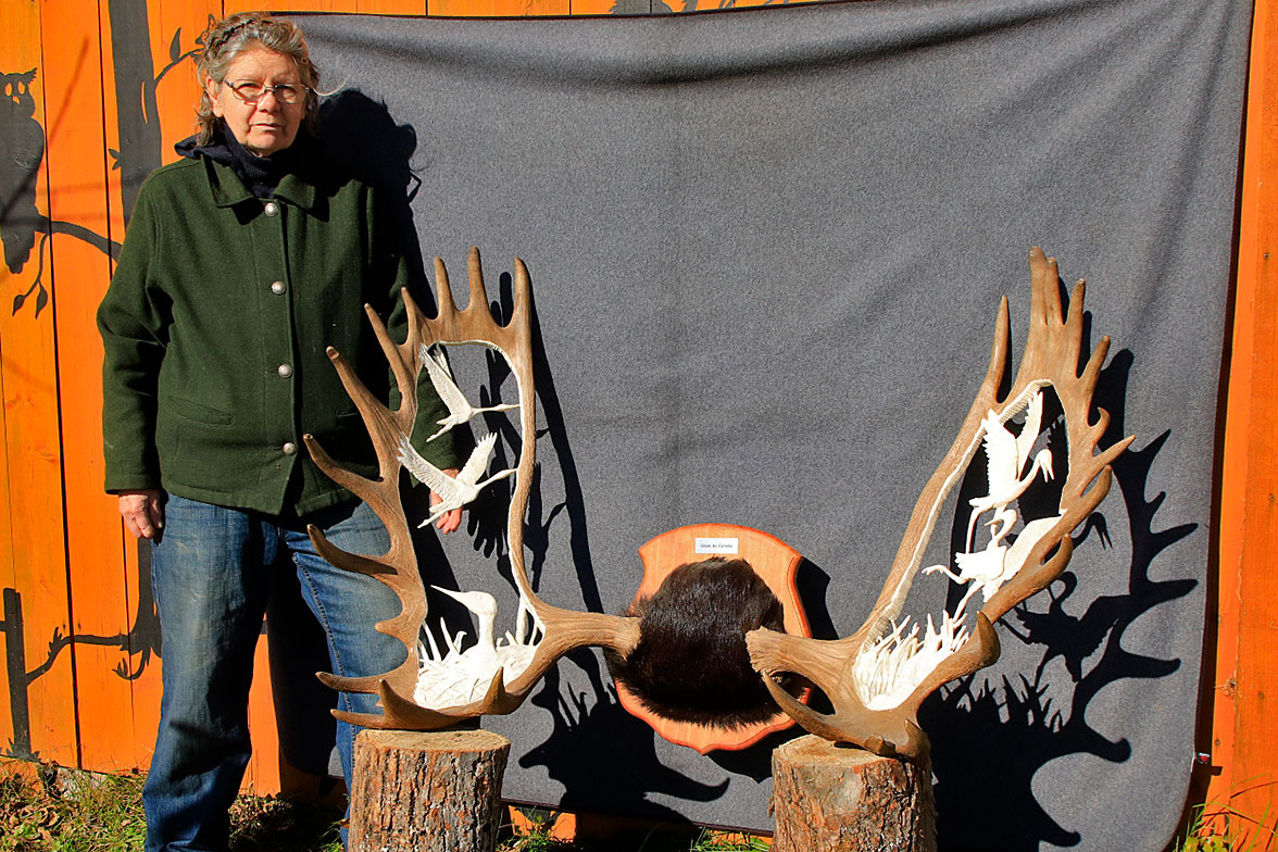 Lynda posant devant une sculpture de grues du Canada réalisée sur panache d'orignal